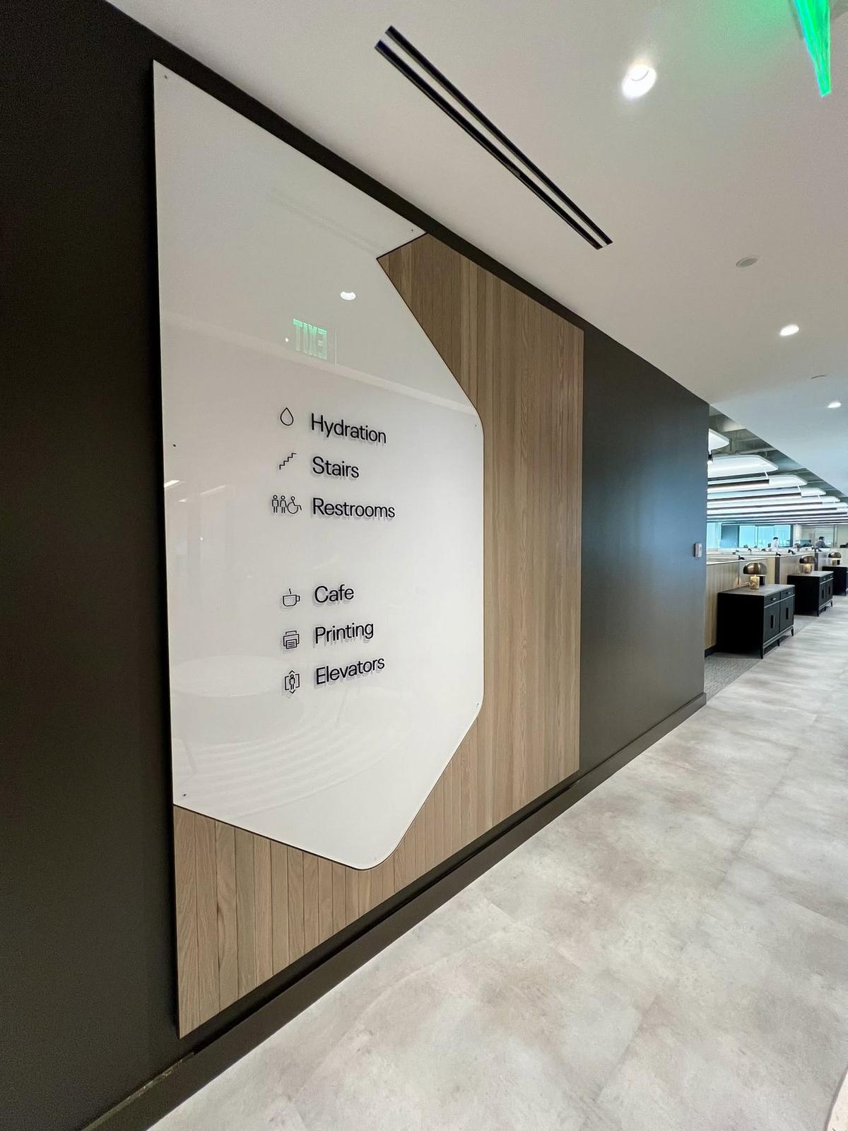 Glass and oak wayfinding panel in a workplace corridor